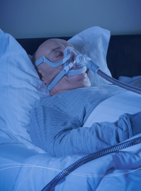 En man som sover i en säng medan han andas via en ventilator.