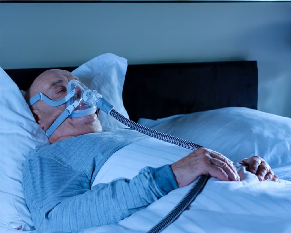 En man som sover i en säng medan han andas via en ventilator.